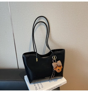 Detail of black faux leather tote bag featuring a cute teddy bear charm and gold hardware