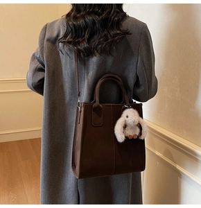Detail of a dark brown tote bag with short handles and a cute white bunny plush pendant