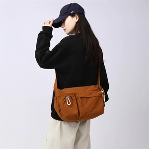 Detail of caramel nylon crossbody bag with dual zip pockets and beaded ornament