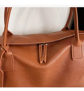 Close-up of smooth two-way metal zippers and embossed logo on brown leather tote bag