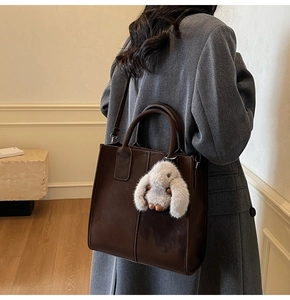 Detail of dark brown leather tote bag with white plush rabbit pendant and shoulder strap