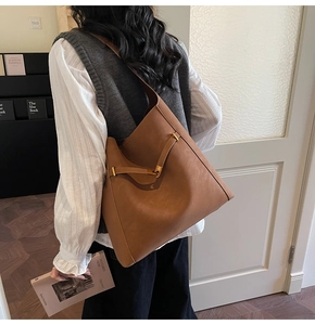 Detail of a large brown leather bucket bag with T-bar metal clasp worn as a crossbody