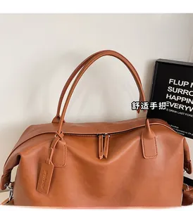 Detail of caramel leather travel bag featuring reinforced handles and embossed brand tag