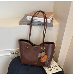 Detail of vintage brown oil wax leather tote bag with a plush puppy charm on a chair