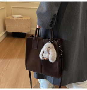 Detail of coffee brown leather tote bag with vertical stitching and plush rabbit charm