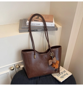 Detail of dark brown oil-wax leather tote bag with metal zipper and cute bear charm