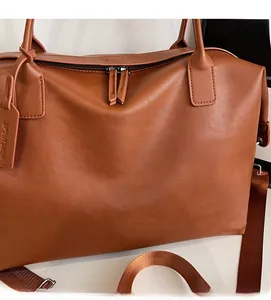 Detailed close-up of a brown leather tote bag with metallic zippers and textured finish