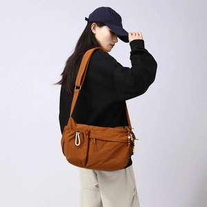 Detail of orange nylon crossbody bag featuring drawstring side pocket and beaded charm