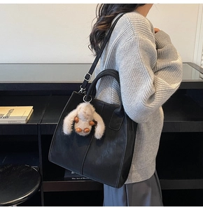 Detail of black leather tote bag with vertical stitching and plush bunny charm