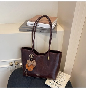 Detail of dark burgundy oil wax leather tote bag with brand logo and cute bear charm