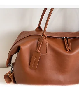 Close-up of brown pebbled leather tote bag detailing handle stitching and zipper brand logo