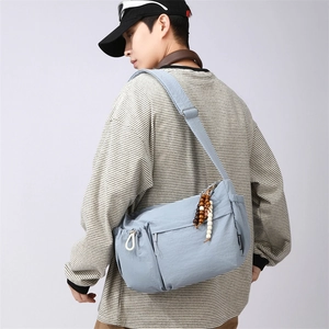 Macro detail of blue nylon crossbody bag with wood bead charm and multiple zipper pockets