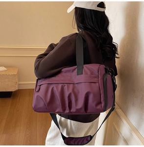 Purple nylon travel bag with shoulder strap shown on model in a modern interior