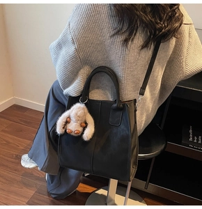 Detail of black leather tote bag with round handles and a plush animal charm