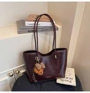 Detail view of burgundy leather tote bag with vintage texture and cute bear pendant