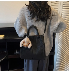 Detail of black faux leather tote bag with plush rabbit charm on a gray sweater