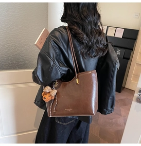 Detail of oil-wax leather tote with a cute bear charm and golden metallic buckle accents