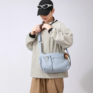 Close-up of light blue nylon crossbody bag featuring multiple pockets and wood bead charm