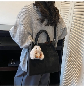Detail of black leather square tote bag with plush bunny pendant shown on a model