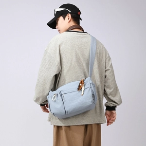 Detail of light blue nylon messenger bag featuring multiple zipper pockets and wood beads