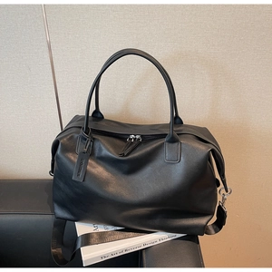 Detail view of black travel tote on a leather chair with adjustable fabric strap