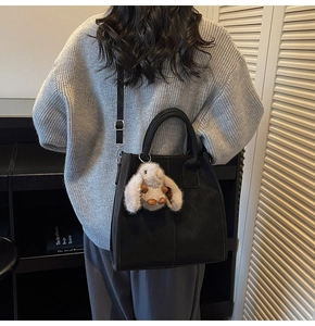 Detail of black tote bag with white plush rabbit charm and adjustable shoulder strap