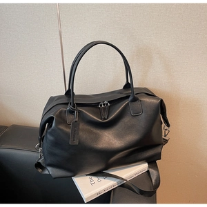Close-up of a black leather travel bag with reinforced handles and brand tag detailing