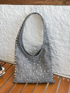 Grey suede tote bag with silver rivet studs on a wooden bench against a white wall