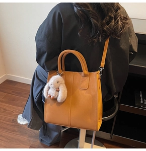 Close-up of caramel tote bag with decorative stitching and a plush bunny charm detail
