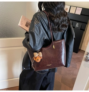 Detail of deep brown glossy leather tote bag with a cute bear charm and golden logo