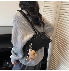 Detail of black suede underarm bag with white stitching and a cute bear charm