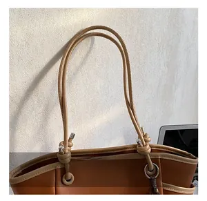 Detail van het bruine lederen tote tas handvat met knoop en zilveren metalen delen