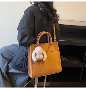 Detail of a large brown tote bag with decorative stitching and a white plush rabbit charm