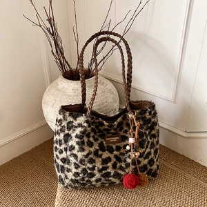 Detail of leopard print plush tote bag featuring woven brown handles and a fluffy red charm