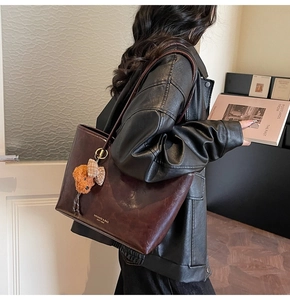 Detail of dark brown wax leather tote with gold logo and plush bear charm on a model