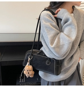 Detail of black suede shoulder bag with white contrast stitching and plush bear charm