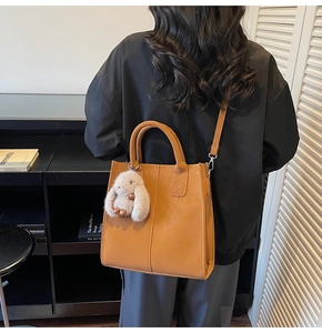 Detail of camel PU leather tote bag with plush bunny charm on a model side view