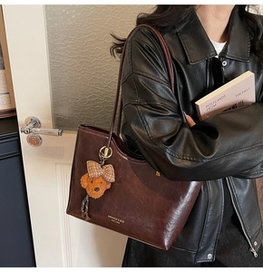 Close-up of retro brown oil wax leather tote bag with cute teddy bear charm and logo