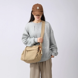 Detail of khaki crossbody bag featuring functional multi-pockets and wooden bead charms