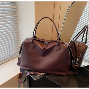 Close-up of burgundy leather travel bag with adjustable strap and silver zippers