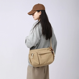 Detail of khaki nylon crossbody bag showing drawstring pocket and wooden bead decoration