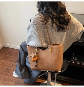 Brown oil wax leather tote bag side view with a cute plush bear pendant and gold logo