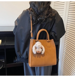 Detail of brown PU leather square bag with white plush rabbit charm on a model's back