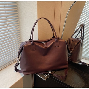 Close-up of a large dark leather tote bag on wood with soft window light and mirror detail