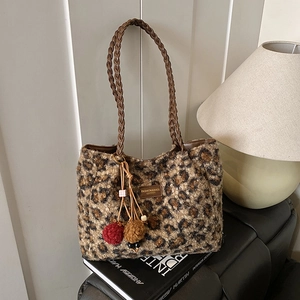 Detailed view of leopard print plush tote bag with woven handles and furry pompom charms