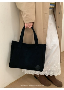 Detail of a black corduroy tote bag showing the vintage style and embossed logo patch