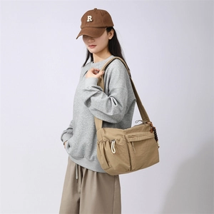 Detail of khaki nylon crossbody bag with side pockets and wood bead tassel accessory