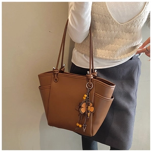 Detailopname van de bruine leren shopper met zijvakken en een decoratieve bloemenhanger