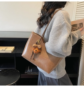 Detail of dark brown oil wax leather tote bag with a cute bear charm on shoulder