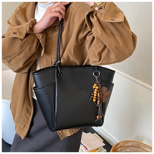 Detail van zwarte leren tote bag met zijvak en etnische houten kralen hanger